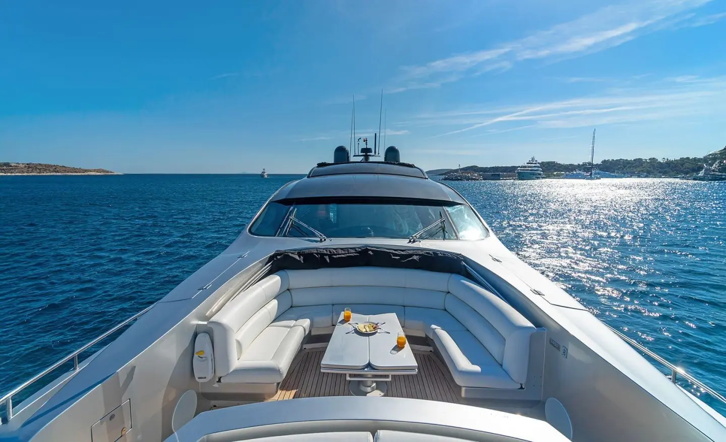 Front deck of a sleek luxury yacht sailing on blue ocean under clear sky