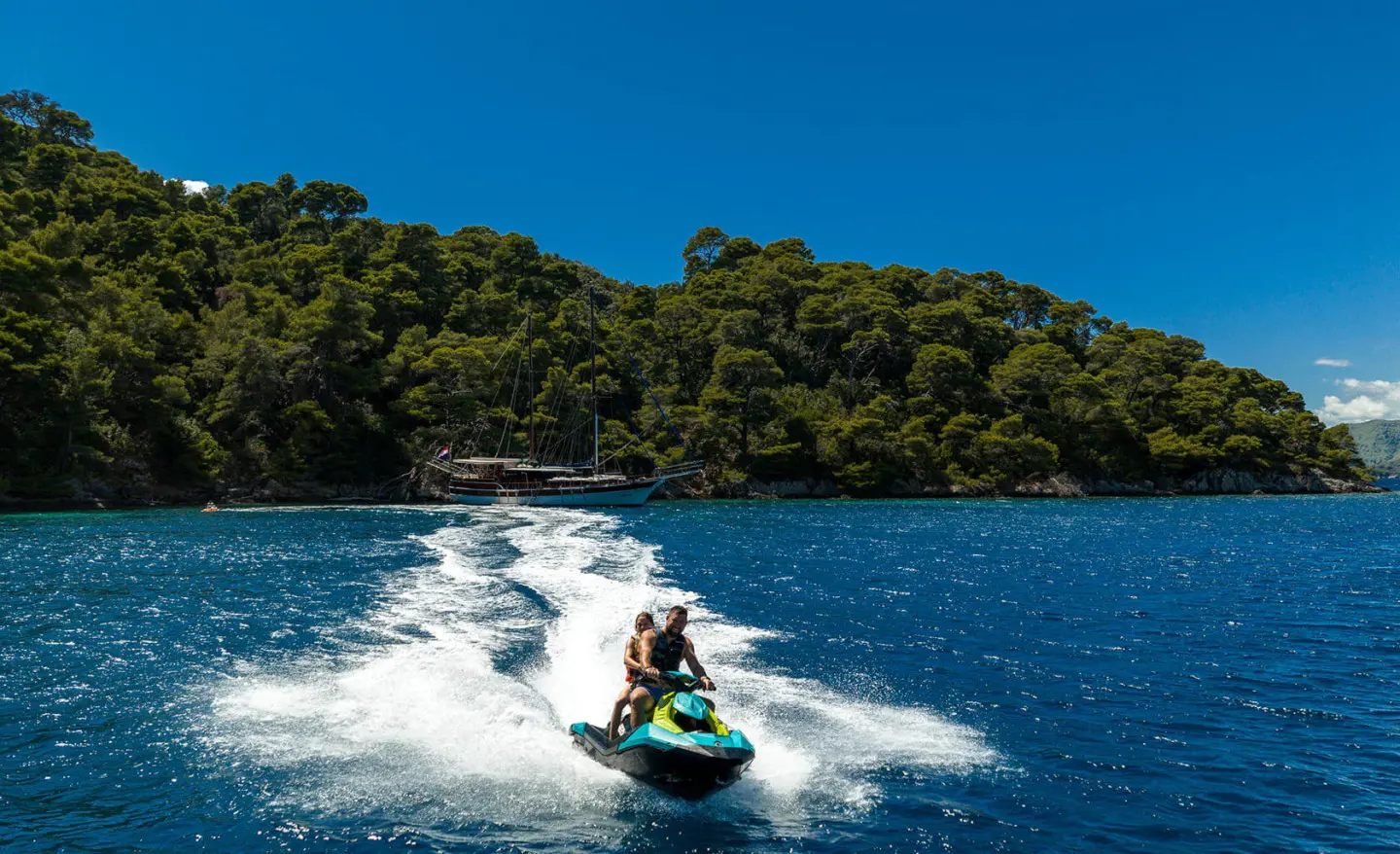 Yacht named Eleganza cruising fast on blue sea; water toys visible