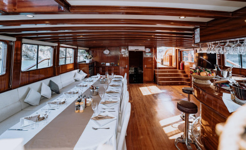 Long dining table with white tablecloth and luxurious wooden interior of the yacht