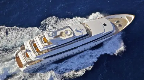 Overhead view of a sleek white luxury yacht cruising blue sea near wake