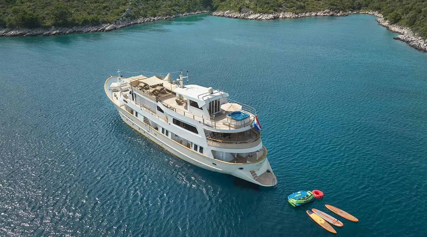 White multi-deck yacht on blue sea near rocky shoreline