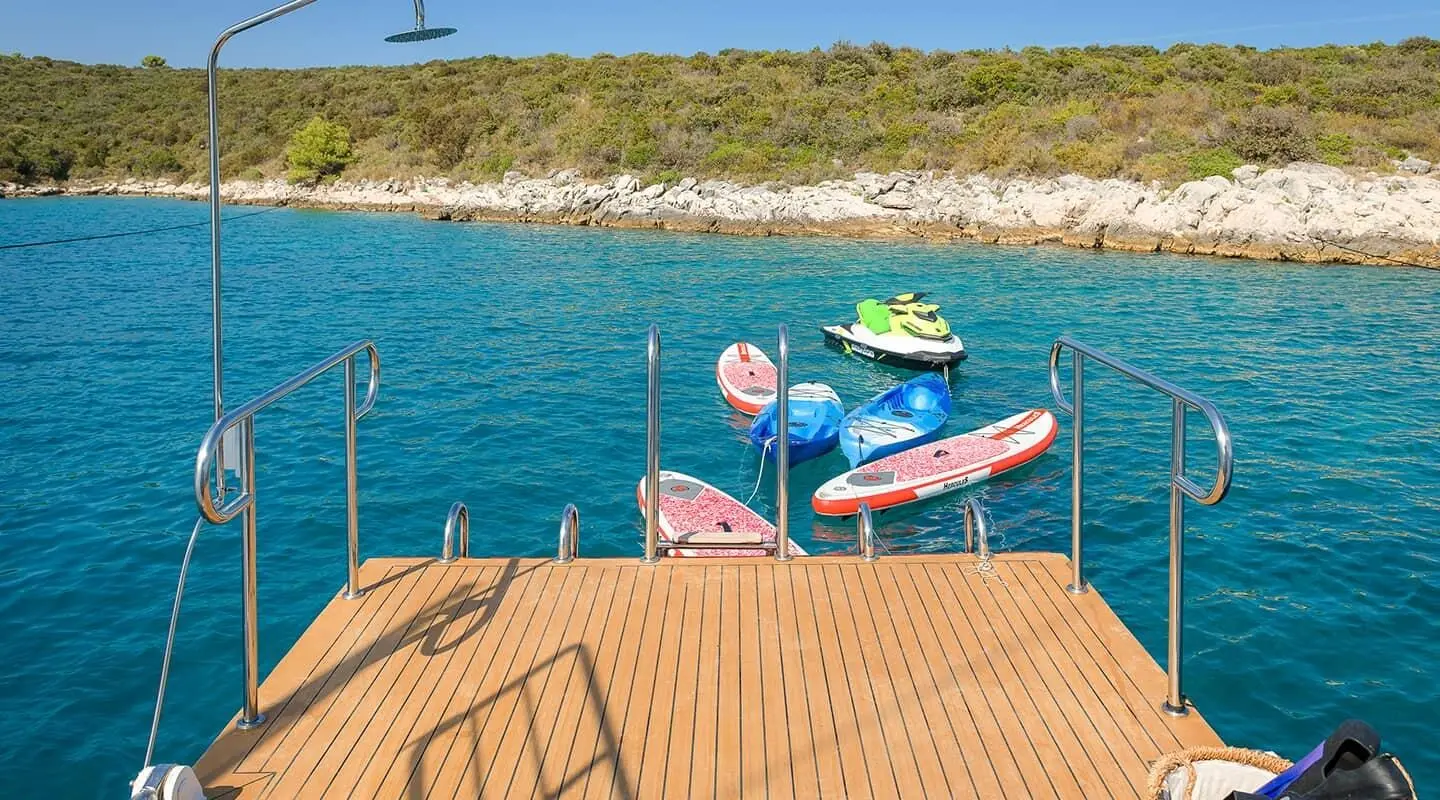 Boat deck railing over turquoise sea with colorful floating boards and jet ski nearby