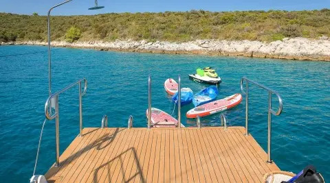 Boat deck railing over turquoise sea with colorful floating boards and jet ski nearby