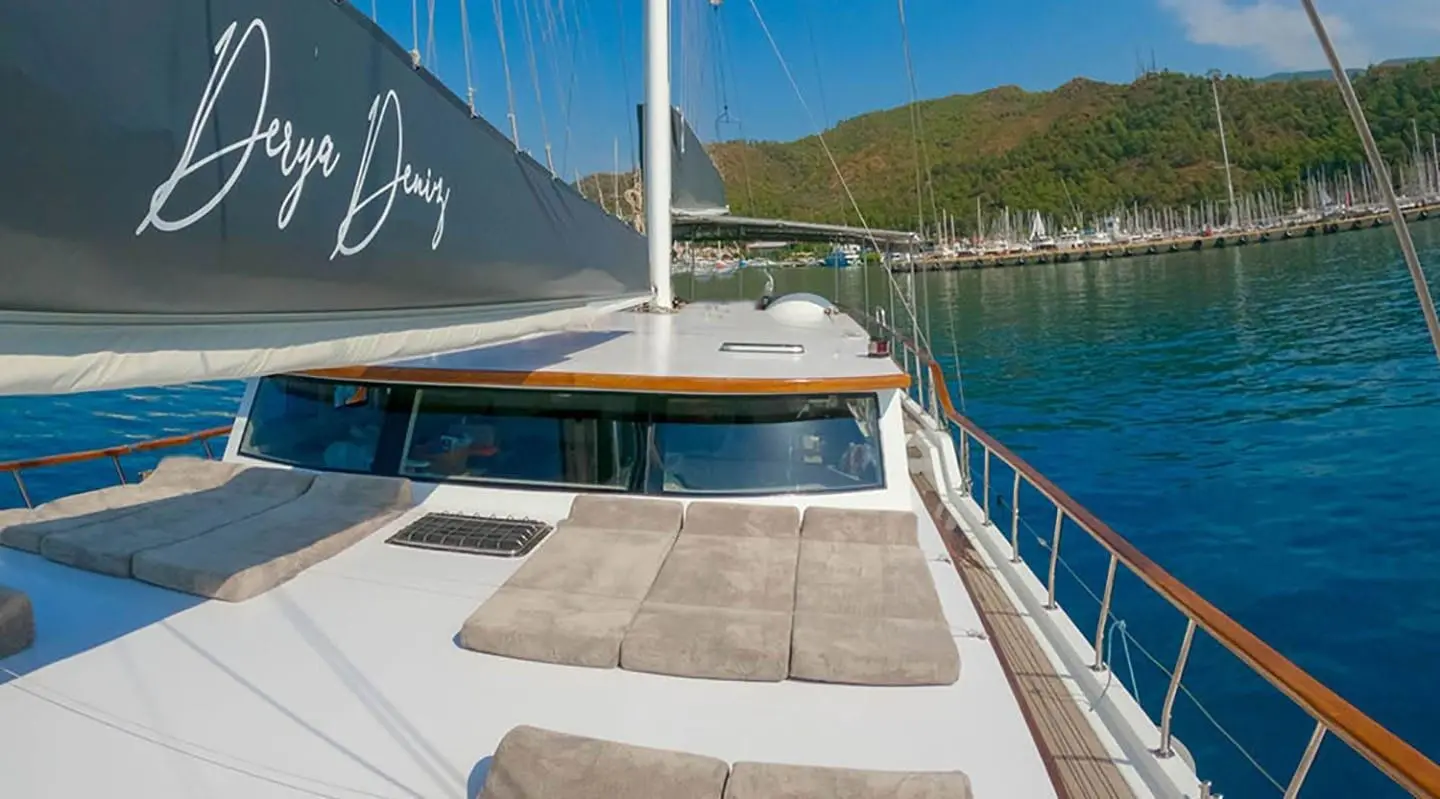 Derya Deniz yacht deck with cushioned seating, sail, and calm blue water at sunset