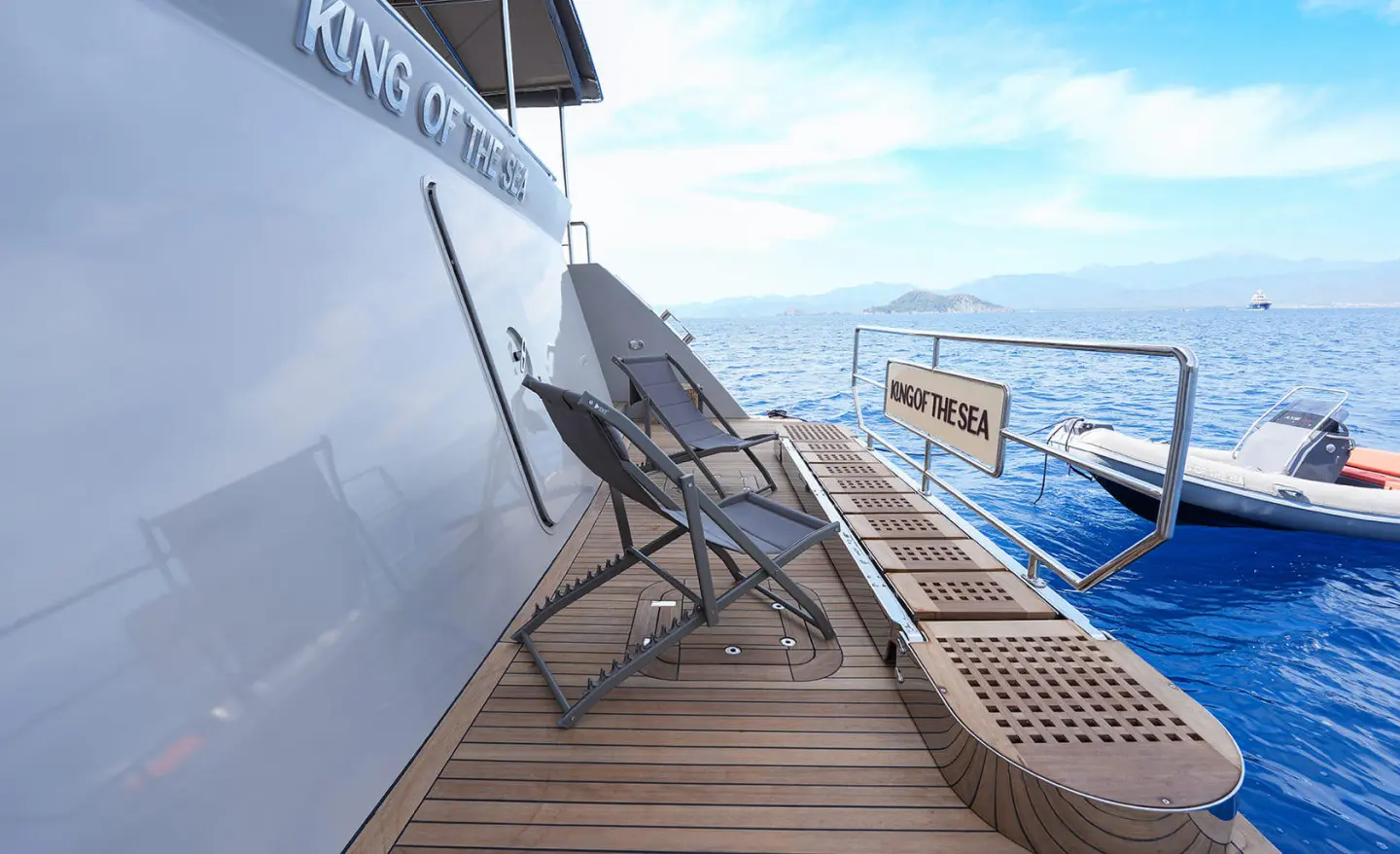 Deck of King Of The Sea yacht with chairs, railing, and ocean view at sunset