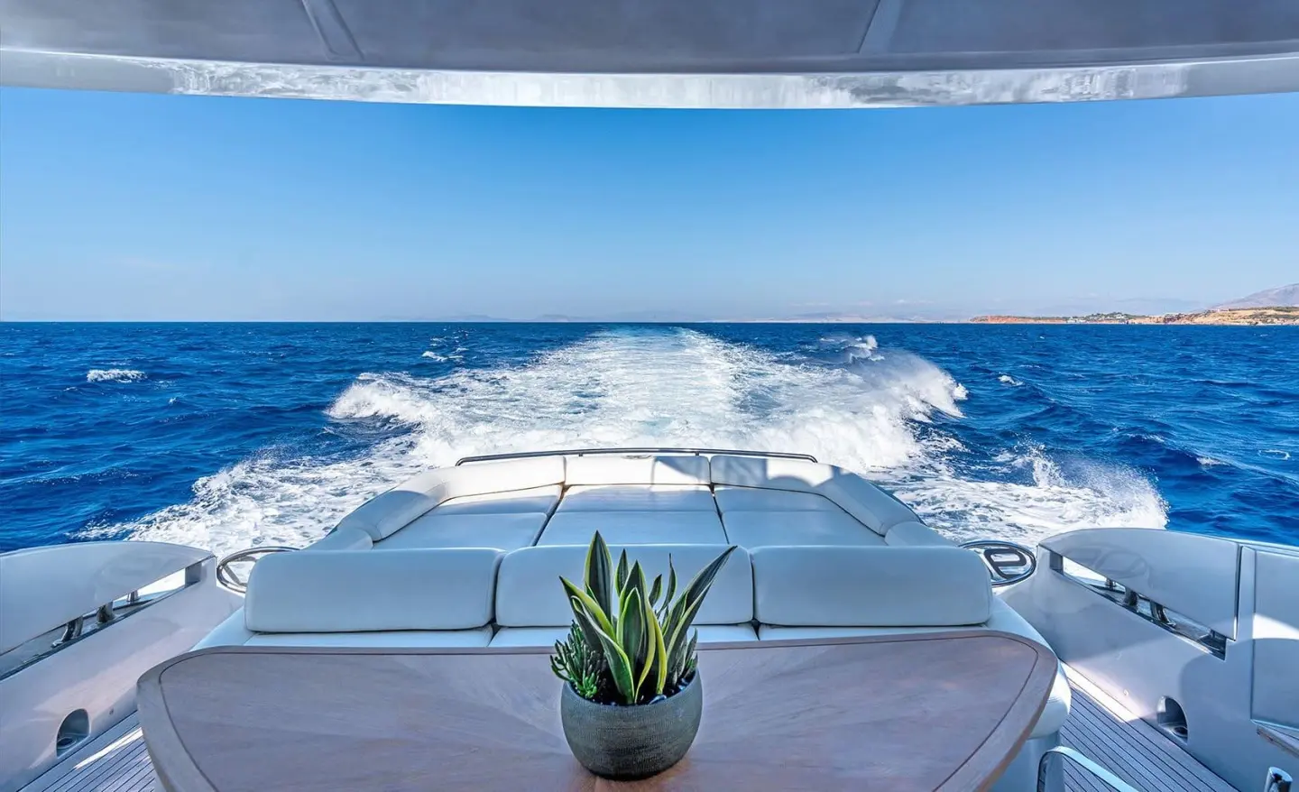 Sunlit yacht deck with calm sea, plant in foreground, ocean view ahead