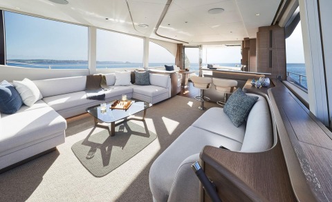Interior of a luxury yacht with white seating, coffee table, and large windows overlooking the sea