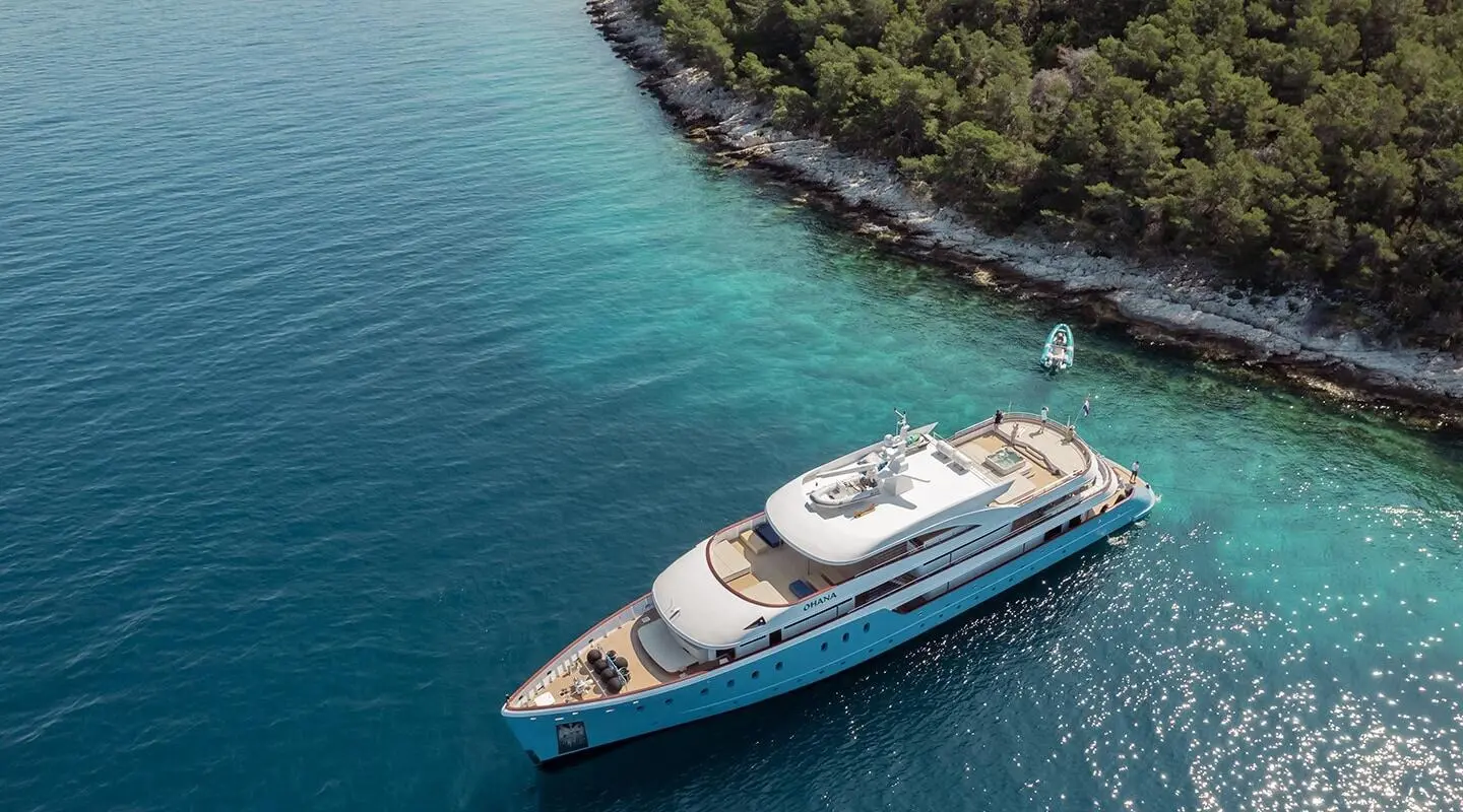 Ohana luxury yacht anchored near rocky coastline at sunset with calm blue water