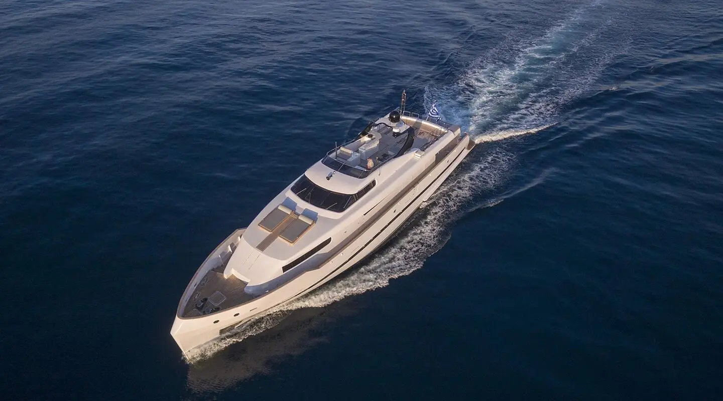 Aerial view of a sleek motor yacht cruising blue sea, wake visible