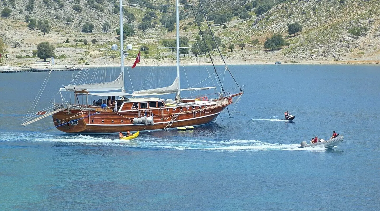 Luxurious wooden gulet cruising coastal blue water at sunset near hillside town