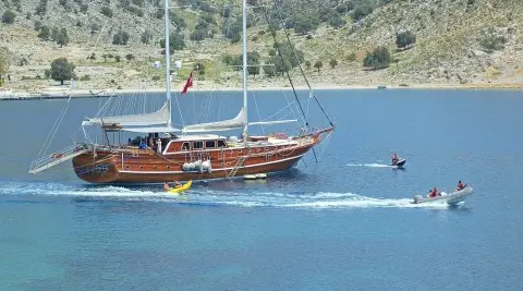 Luxurious wooden gulet cruising coastal blue water at sunset near hillside town