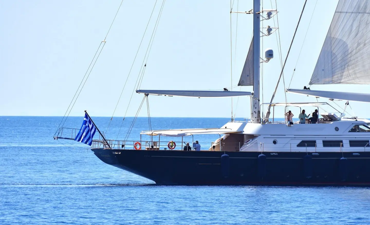 Blue sailing yacht Tamarita anchored with sails up and crew on deck