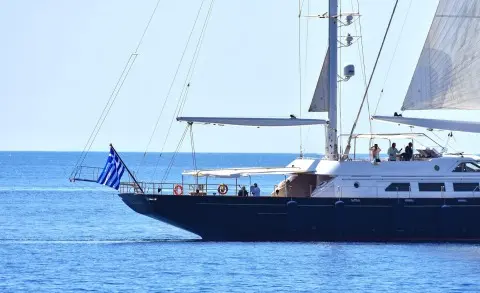 Blue sailing yacht Tamarita anchored with sails up and crew on deck