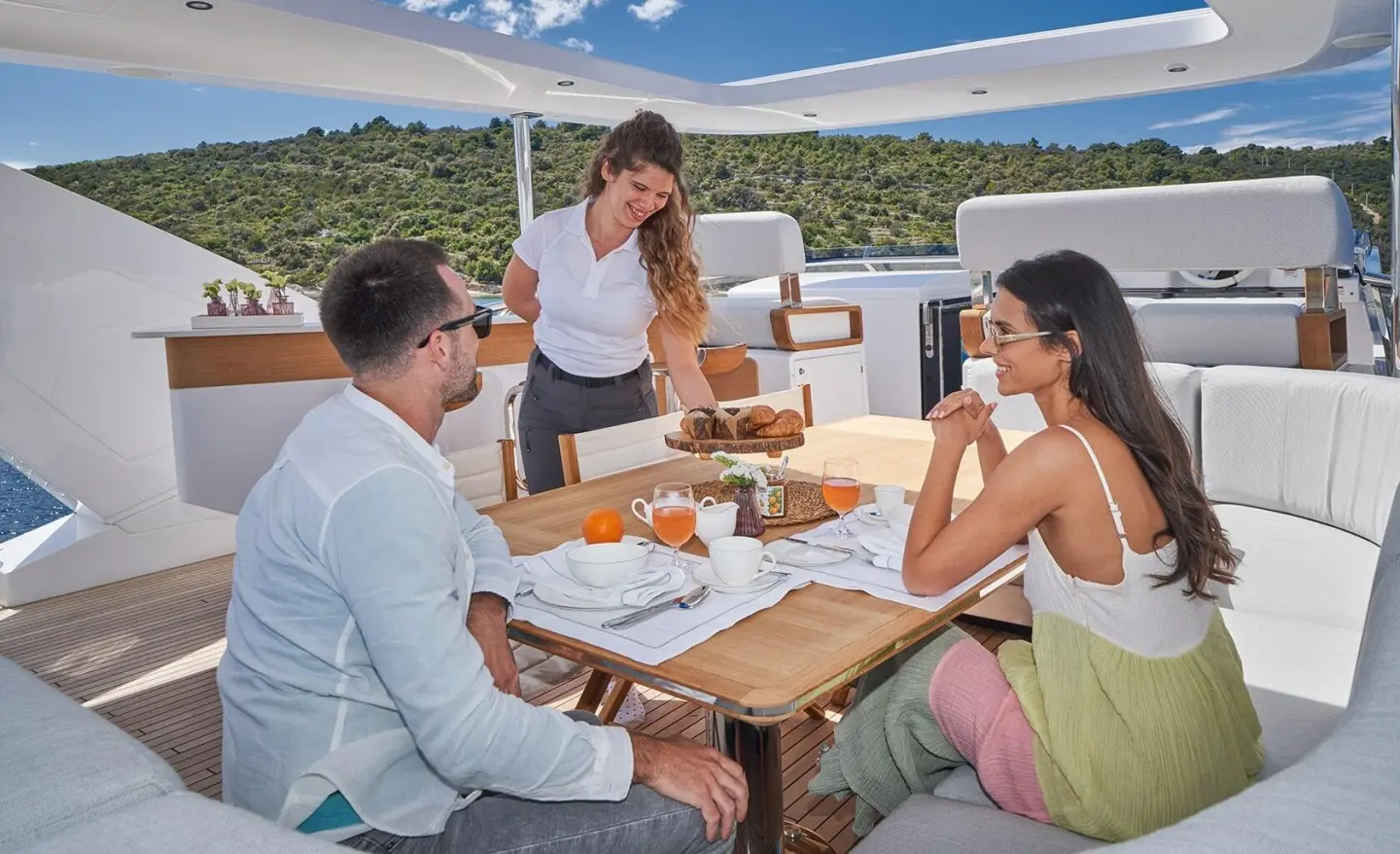 Group of people dining on a yacht at sunset with wooden table and plates