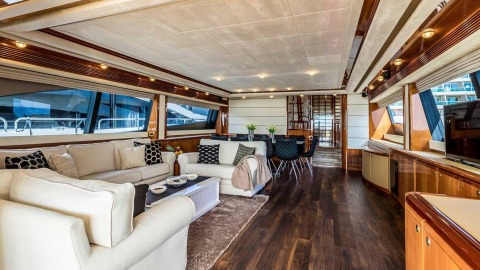 Luxurious motor yacht interior with white sectional sofas, decorative cushions, dark wood floor and large windows