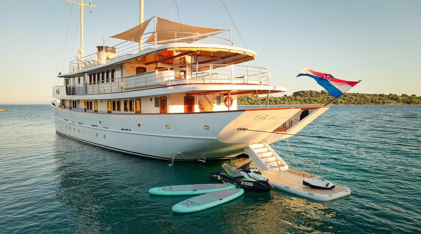 Yacht Bellezza anchored with sunlit deck, white hull, and orange shade sails nearby
