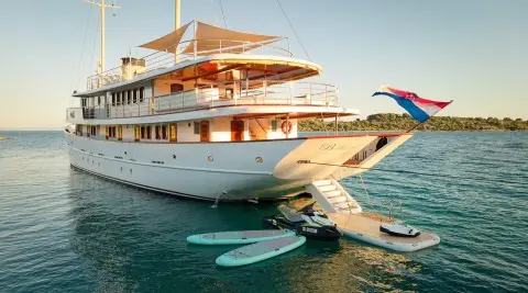 Yacht Bellezza anchored with sunlit deck, white hull, and orange shade sails nearby