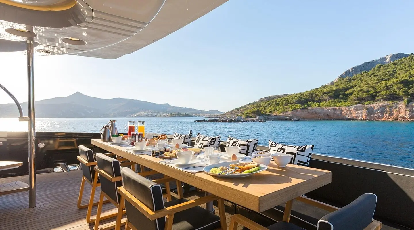 Luxury yacht dining on deck at sunset with wooden table and seaside view