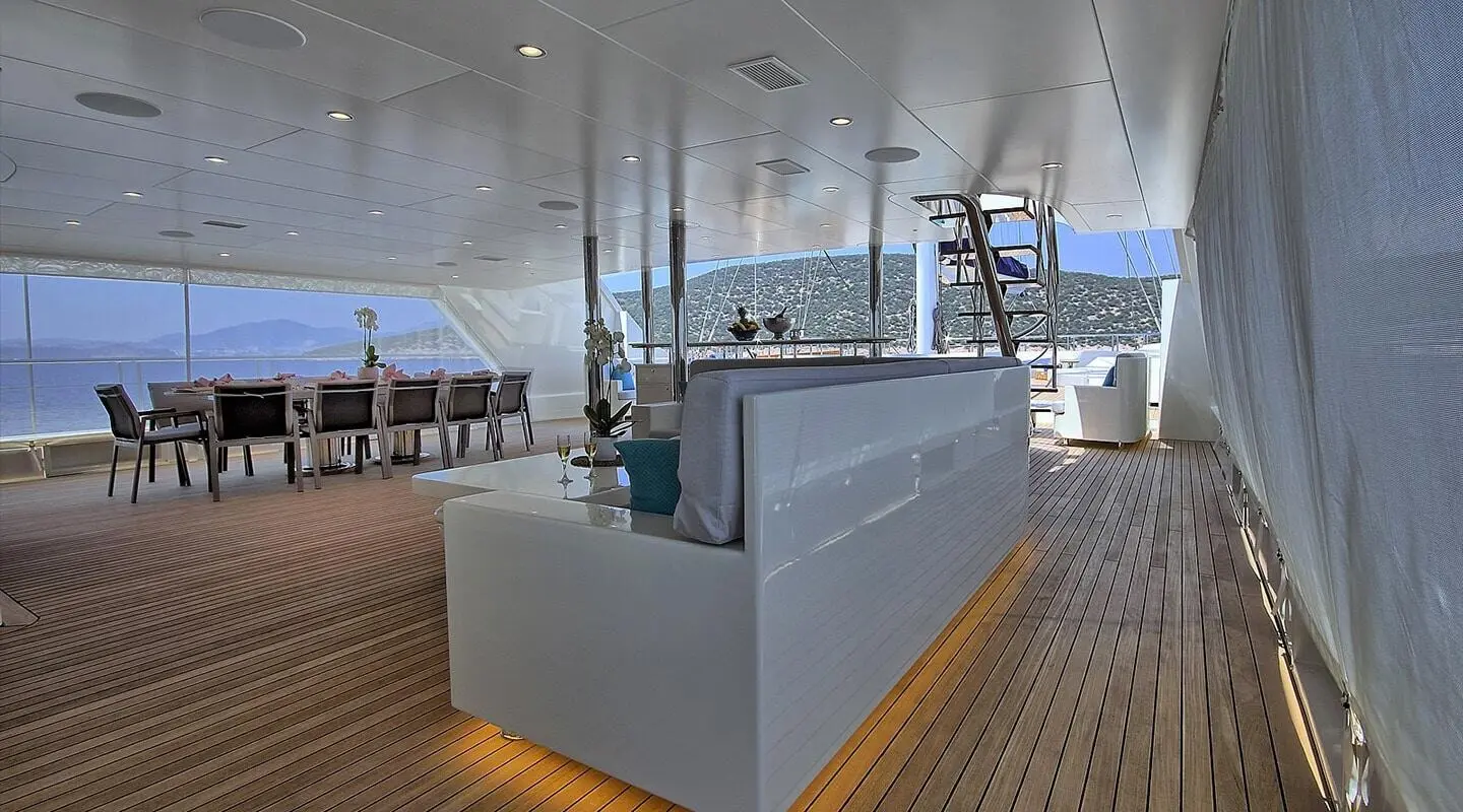Meira yacht lounge area with seating, glass railing, and wooden deck under clear sky