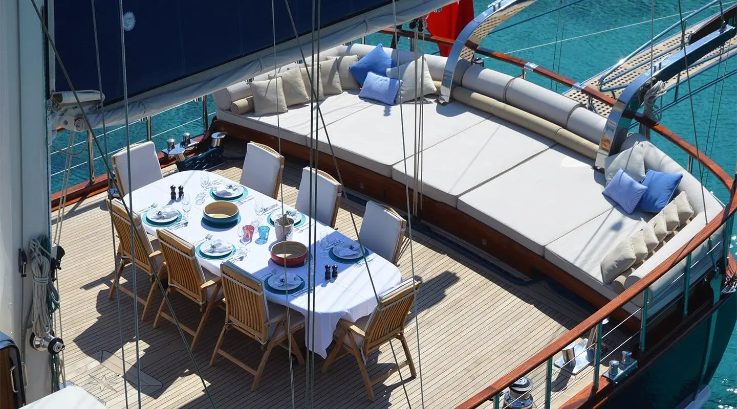 Aft dining table on a gulet with blue cushions and wooden deck seating