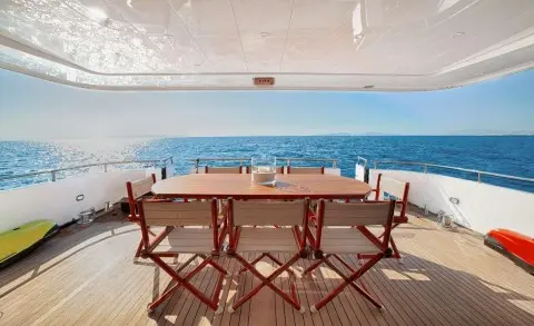 Dining deck on luxury yacht Zoi with wooden table and chairs overlooking sea