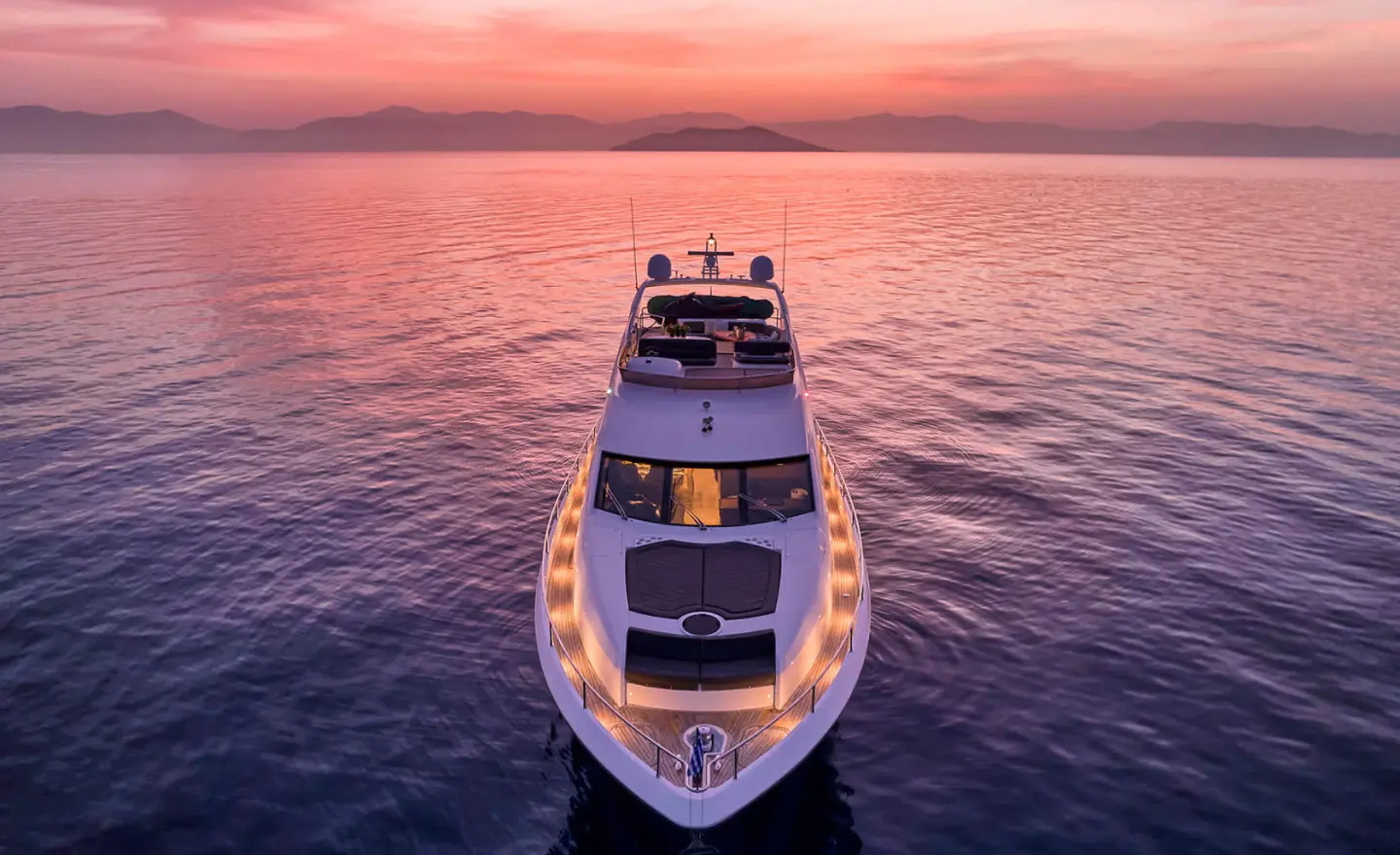 Top-down view of M Five yacht sailing at sunset, calm water and pink sky
