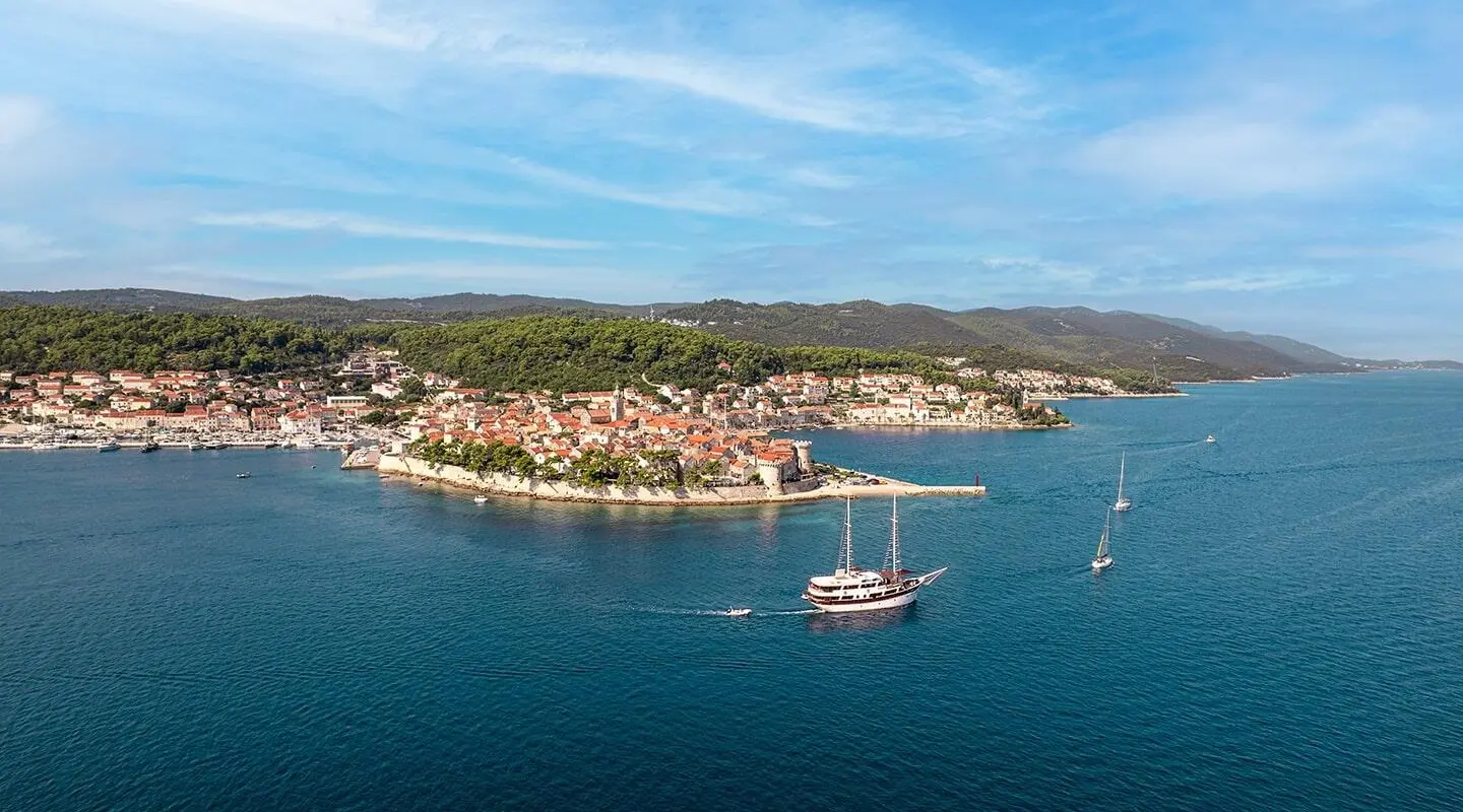 Gulet Cesarica yacht anchored near coastal town with calm blue sea.