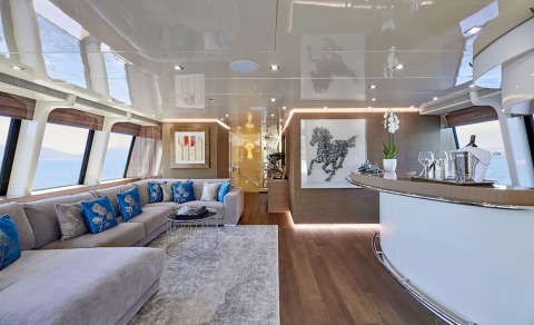 Daloli yacht interior: spacious salon with L-shaped sofa, blue accent pillows, and large windows