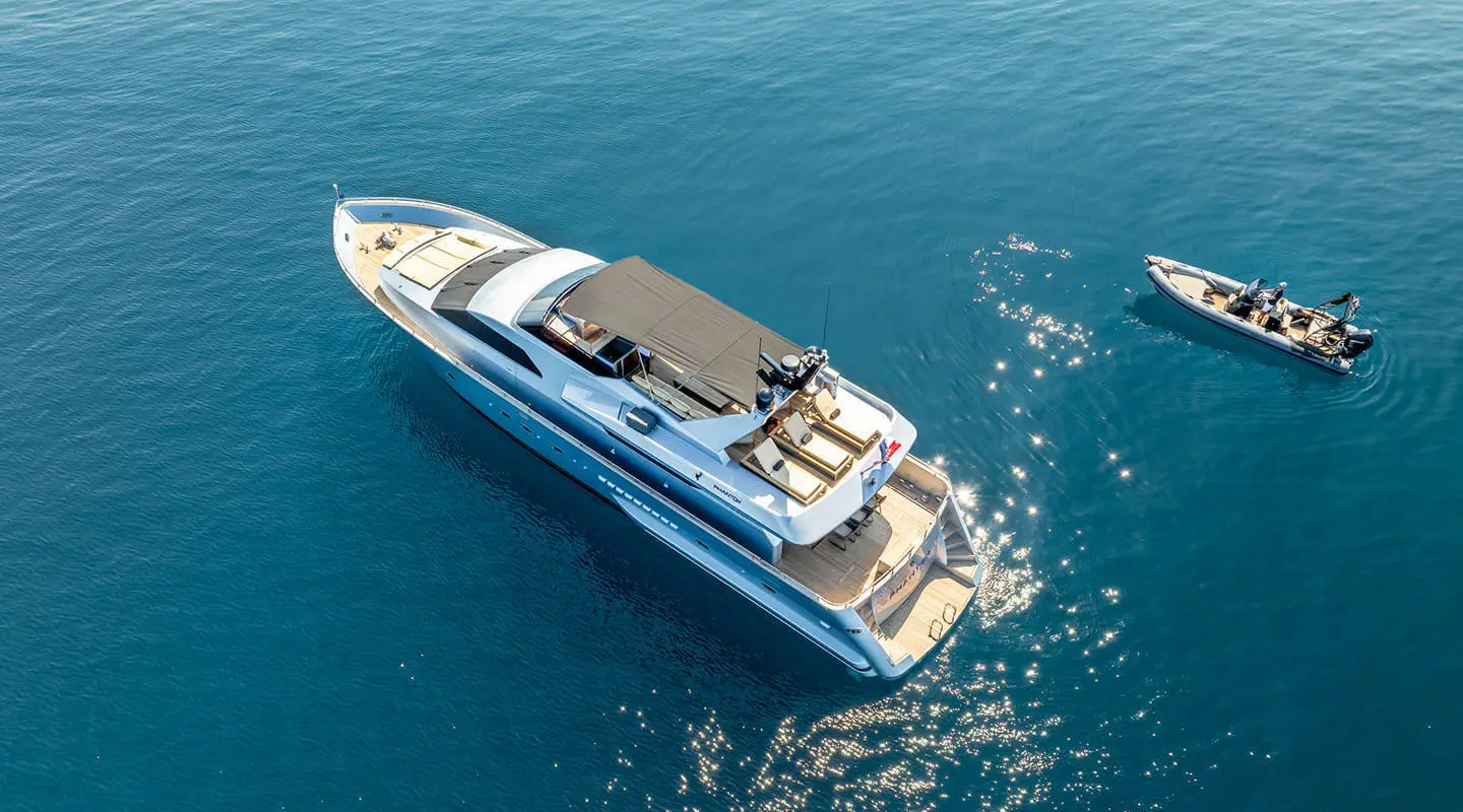 A blue and white Phantom motoryacht anchored in calm blue water from an aerial view