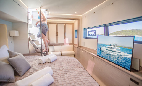 Bed interior with pillows and quilted bed in foreground; TV and windows showing sea view in background