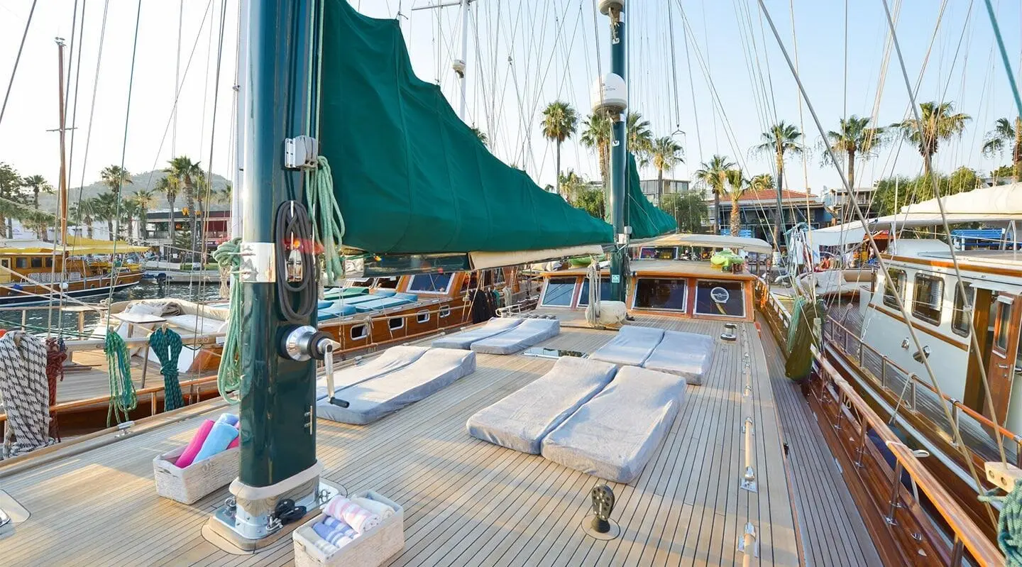 Ros Mare yacht deck with ropes, sails, and marina in twilight light