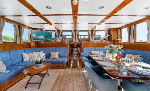 Interior of a yacht with blue seating, wooden panels, and a dining table set for a meal