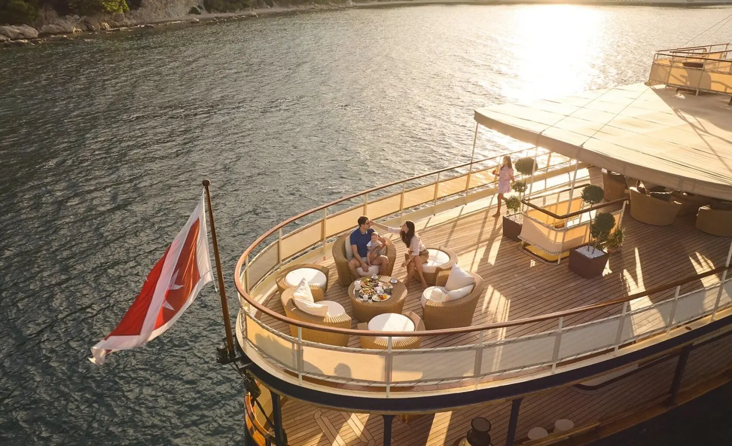 People seated on a luxury outdoor deck lounge on a yacht with seating area by the water