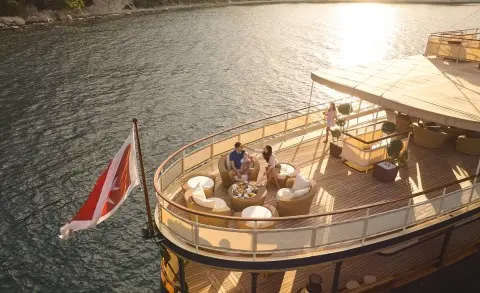 People seated on a luxury outdoor deck lounge on a yacht with seating area by the water