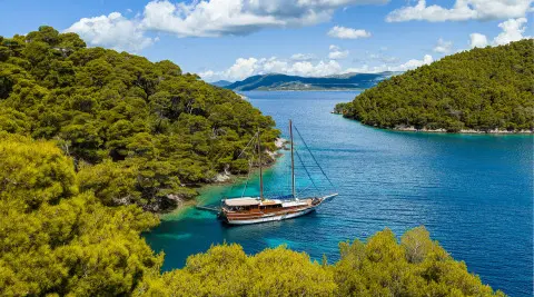 Eleganza yacht anchored in turquoise cove between green cliffs at sunset