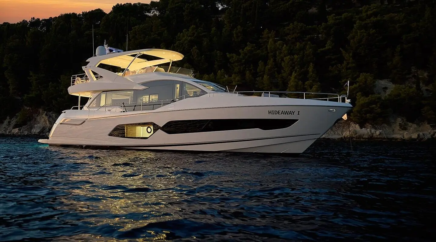 Sleek white luxury yacht named Hideaway anchored on calm water at dusk