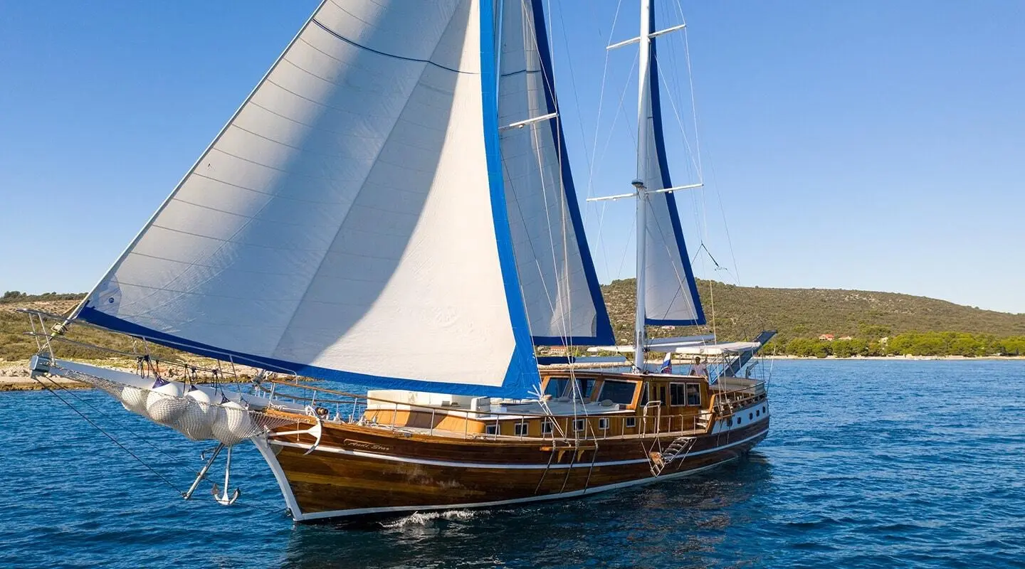 Andi Star luxury 26m sailing yacht with white and blue sails anchored in clear blue seas