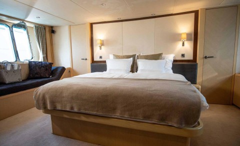 A bedrooms with a large bed, wall lamps, and wooden cabinets; window with curtains on the side.