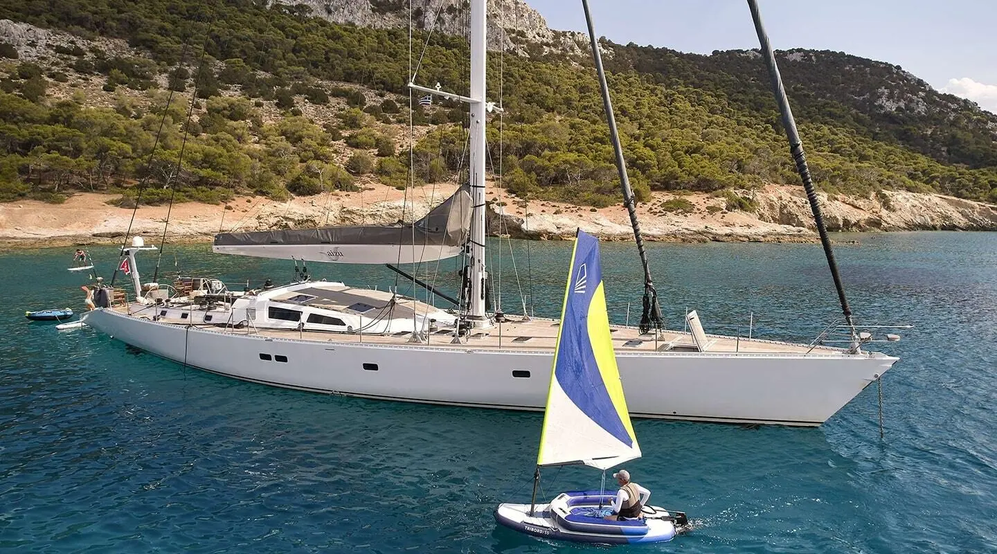 Small sailboat near a larger white motor yacht named Aizu at calm coastal waters