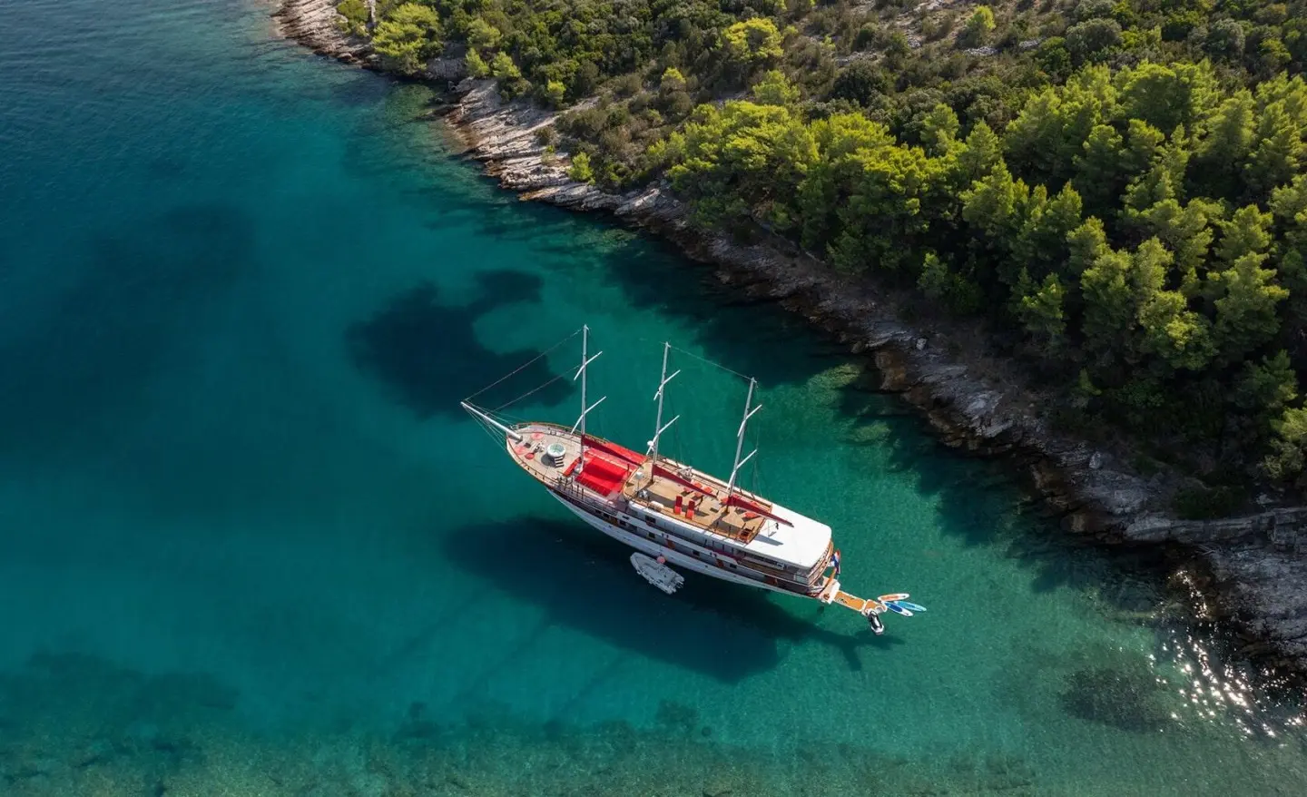 Aerial view of Barbara yacht anchored in clear turquoise water near green shoreline