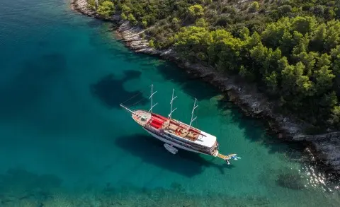 Aerial view of Barbara yacht anchored in clear turquoise water near green shoreline