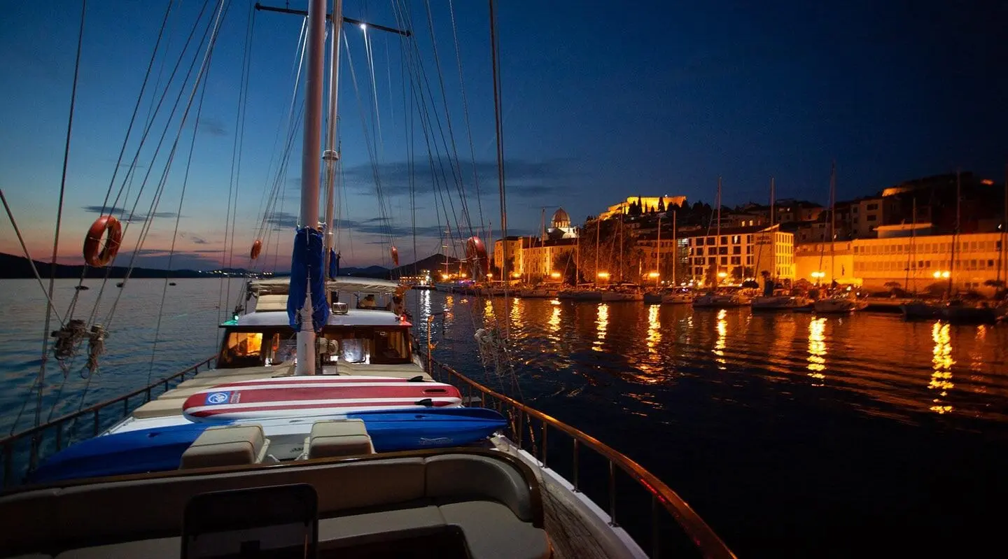 Malena yacht moored at dusk with illuminated harbor buildings reflecting on calm water