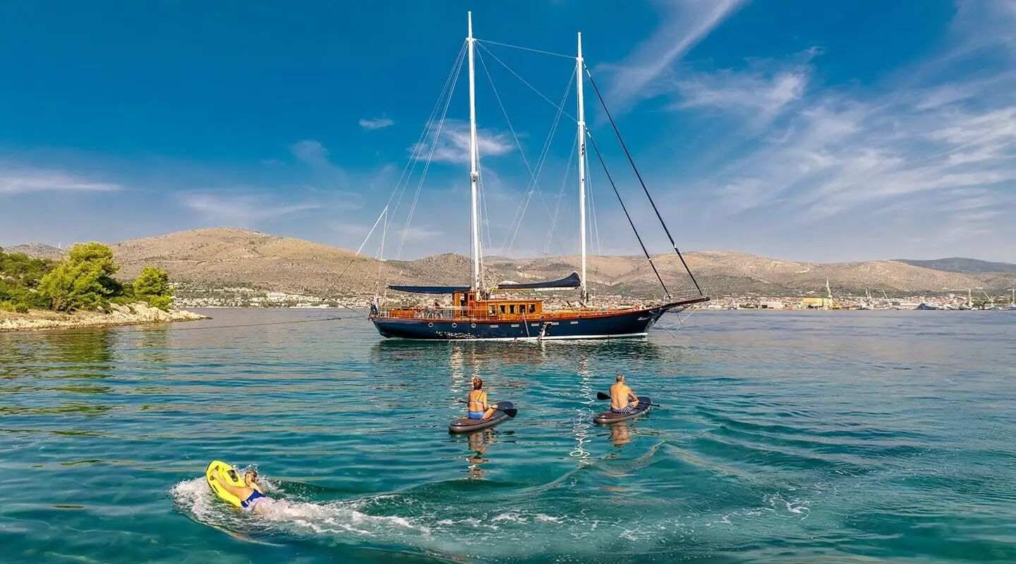Smart Spirit yacht anchored in clear turquoise water at sunset, sails down