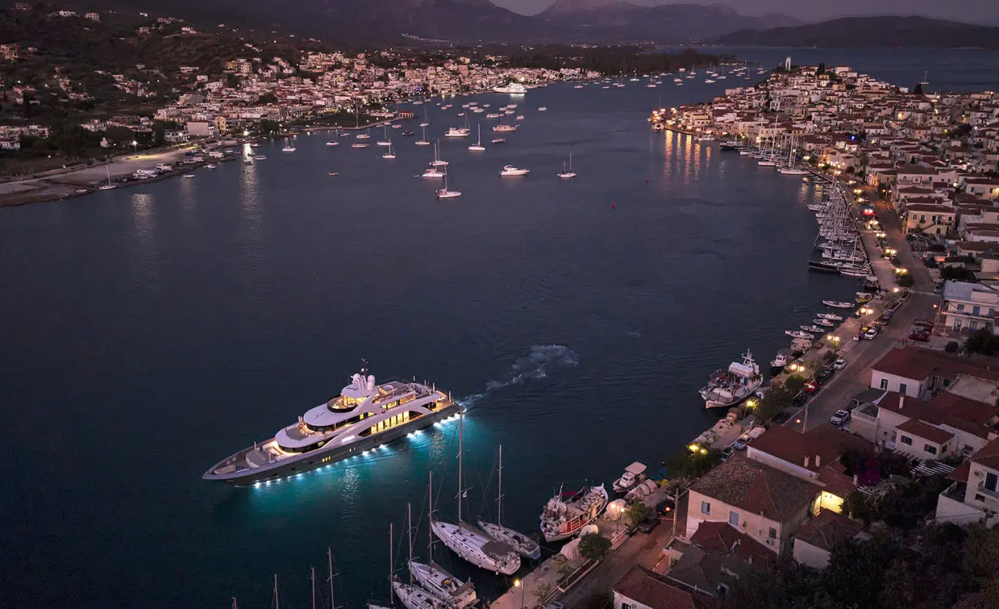 Luxurious yacht La Pellegrina 1 sailing in a harbor at night with lit coastal town