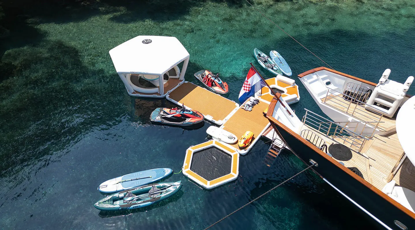 Maia yacht anchored near turquoise water with a yellow floating dock and dinghies nearby