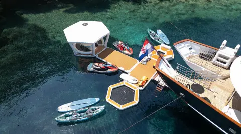 Maia yacht anchored near turquoise water with a yellow floating dock and dinghies nearby