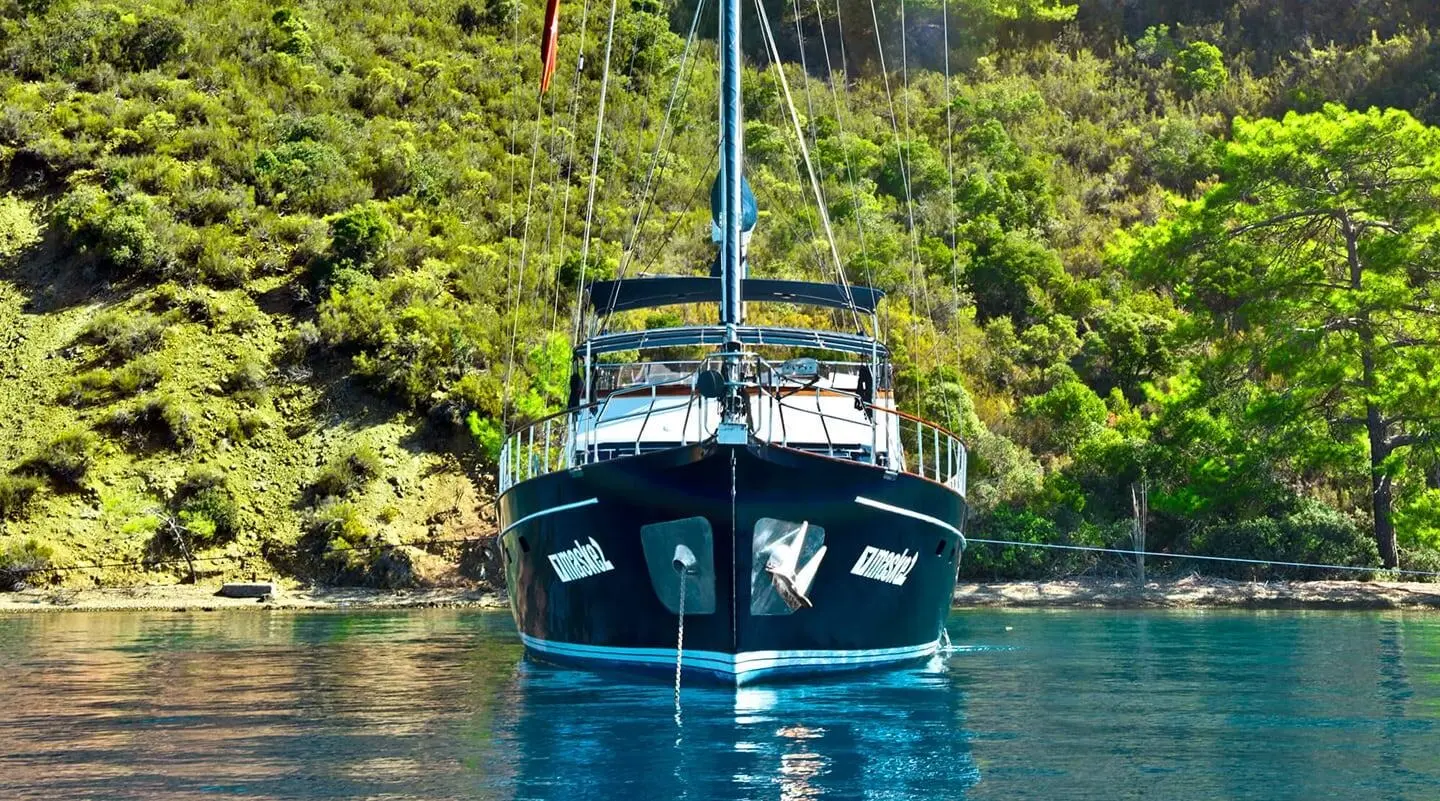 Maske 2 yacht anchored in calm water with lush green shoreline in view