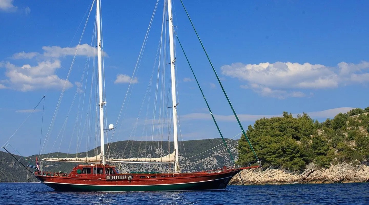 Carpe Diem 7 luxury gulet sailing at sunset, anchored by rocky shoreline