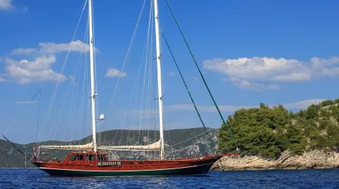 Carpe Diem 7 luxury gulet sailing at sunset, anchored by rocky shoreline