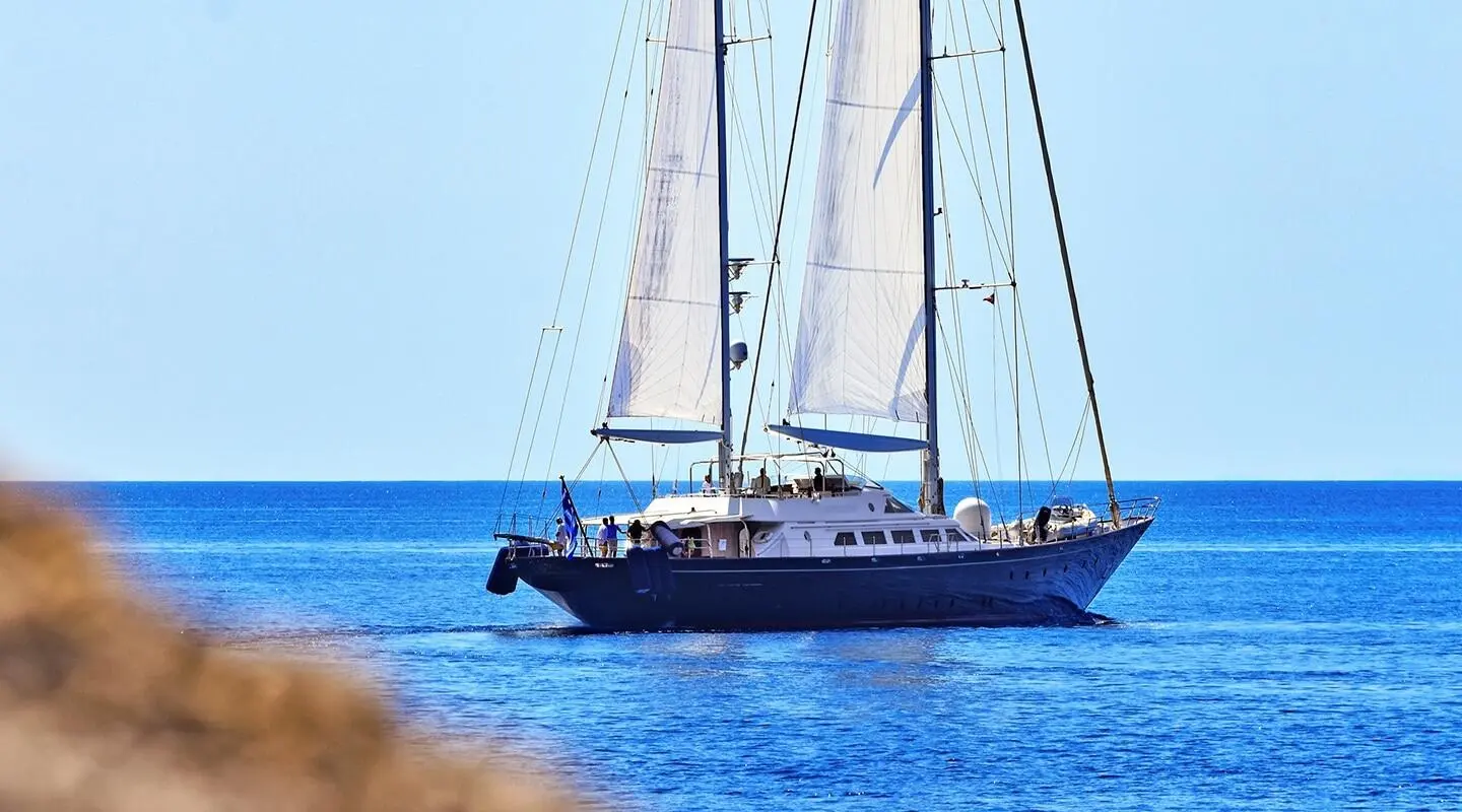 Yacht Tamarita anchored with sails raised, blue sea and clear sky